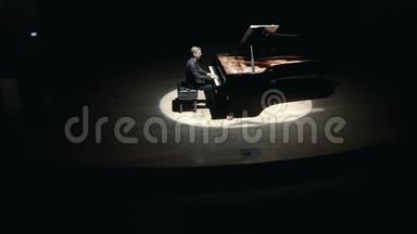 舞台上的大钢琴：一个穿着黑色西装的优雅男子在音乐厅的舞台上演奏大钢琴